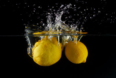 Falling lemons in water, spray for design, freezing in motion. Water splash and vegetables isolated on a black backgroud Imagen De Limones Cayendo Al Agua, Desinfección En Tina Con Ozono